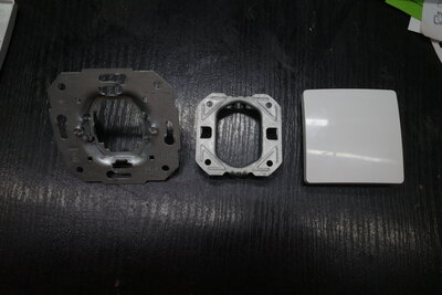 Aus diesen verbleibenden Teilen habe ich die Blindabdeckung gebaut. Das große Metallteil ist natürlich gut darin, in einer Elektrodose zu halten. Dafür wurde es gebaut. Das kleine Metallteil hält fest am anderen, wenn man es einsetzt. Und die Die ehemalige Schalterwippe, jetzt Dosenabdeckung, schließt das ganze optisch ab.